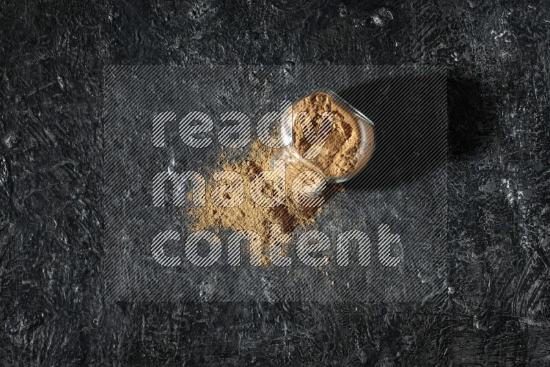 وعاء زجاجي للتوابل مقلوب ممتلئ ببودرة بهار الفلفل الحلو والبودرة تناثرت منه على خلفية سوداء