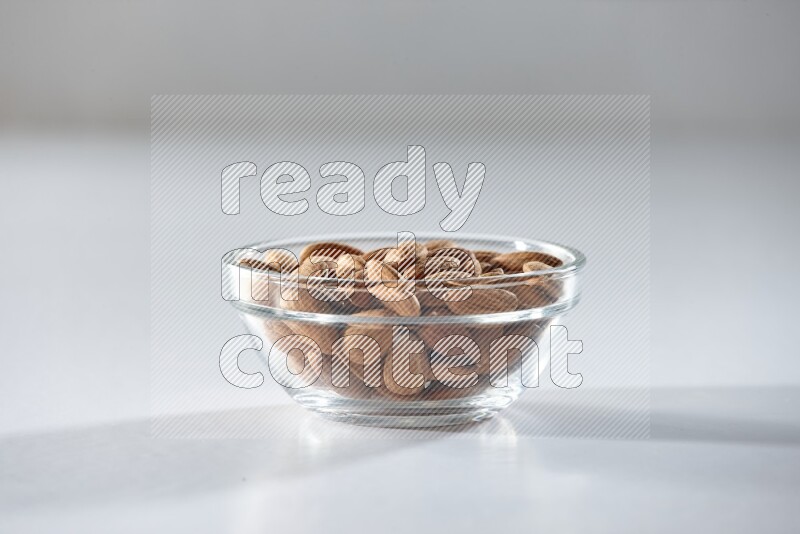 A glass bowl full of peeled almonds on a white background in different angles