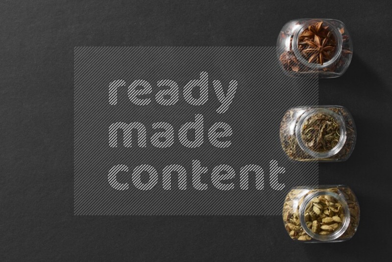 يانسون نجمي وريحان مجفف وحبوب الهيل في أوعية زجاجية علي خلفية سوداء