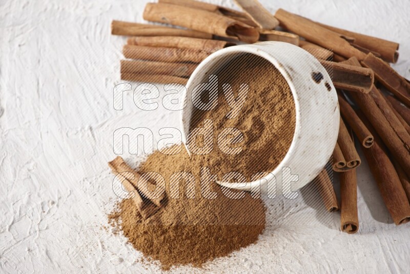 Ceramic beige bowl over filled with cinnamon powder and cinnamon sticks around the bowl on a textured white background in different angles