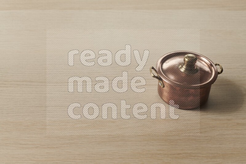 A small copper pot on light wooden background