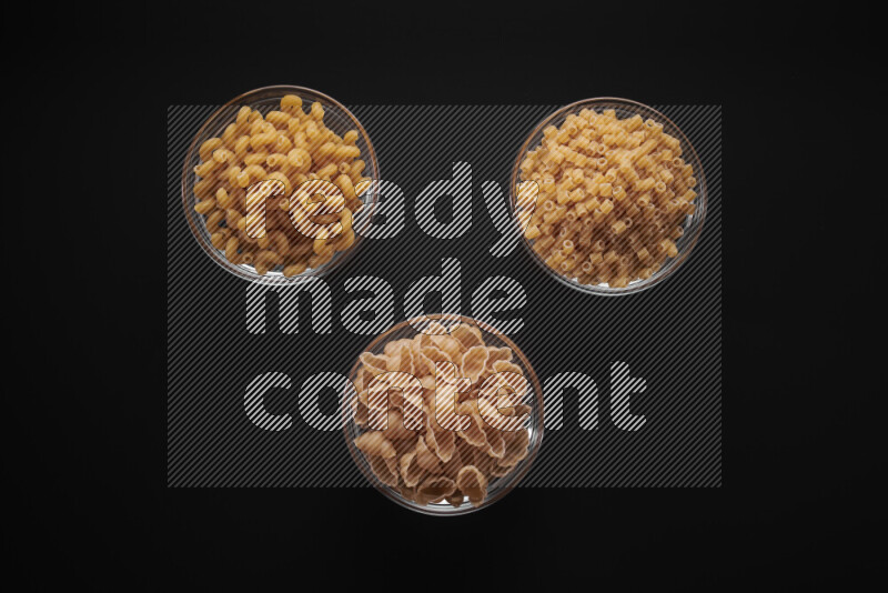 Different pasta types in glass bowls on black background