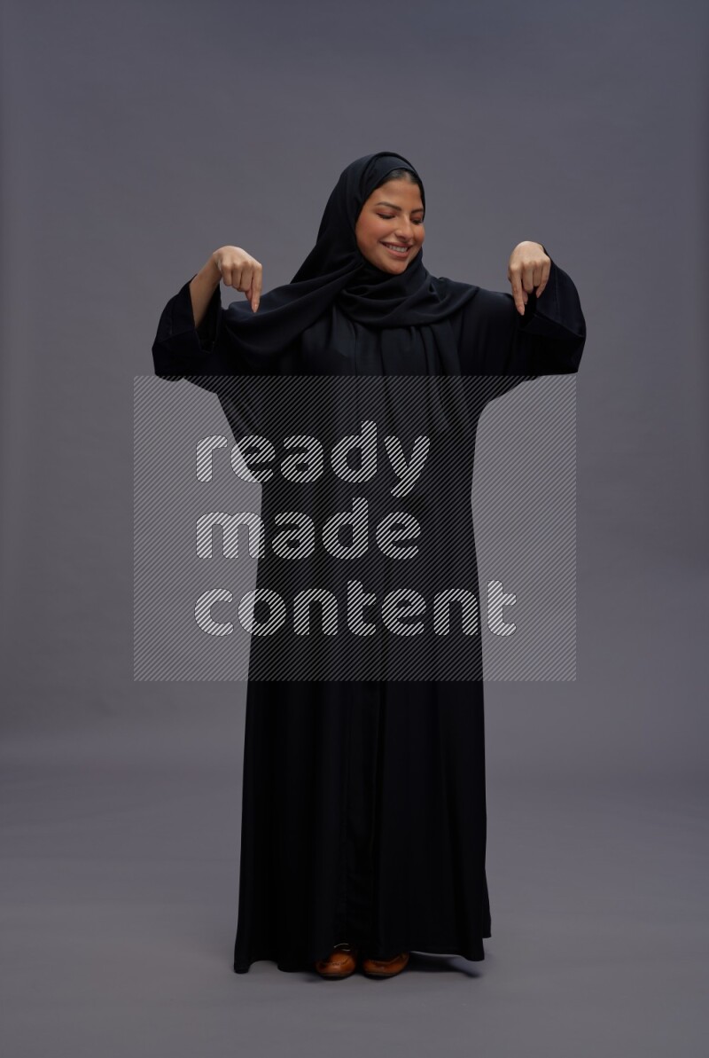Saudi woman wearing Abaya standing interacting with the camera on gray background