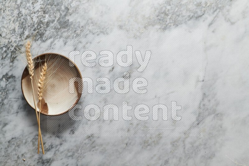 Wheat stalks on multicolored pottery plate on grey marble background