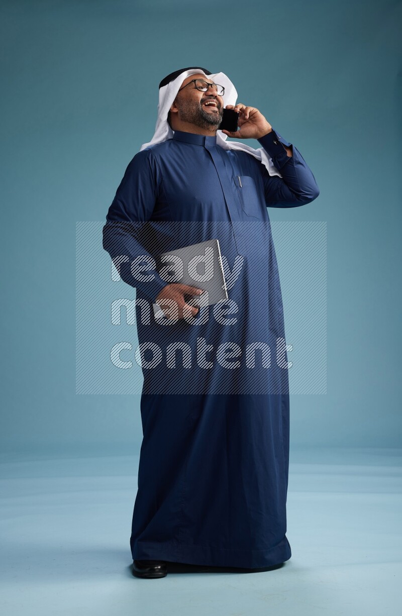 Saudi Man with shimag Standing talking on phone on blue background