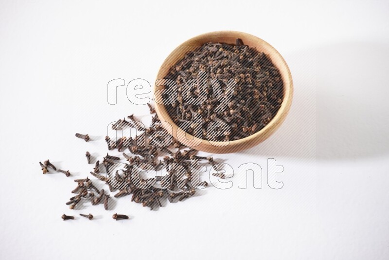 A wooden bowl full of cloves with spread grains on a white flooring