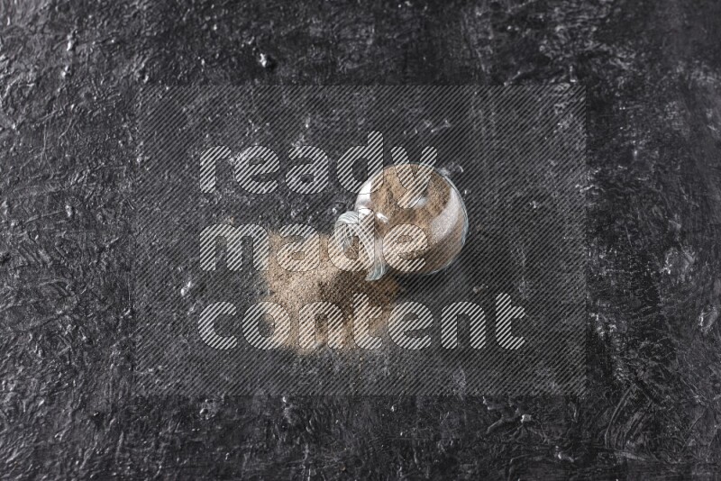 بودرة الفلفل الأسود في وعاء زجاجي مقلوب علي خلفية سوداء