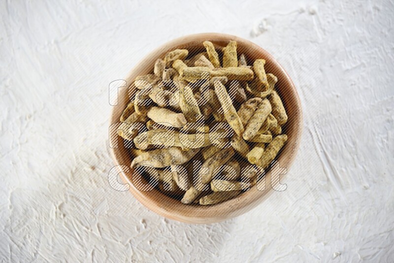 وعاء خشبي ممتلئ بأصابع الكركم المجفف على خلفية بيضاء