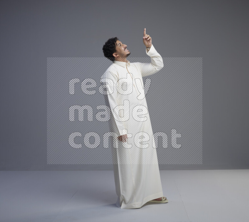 A Saudi man standing wearing thob interacting with the camera on gray background