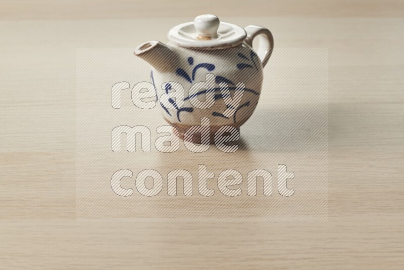 A pottery teapot on light wooden background