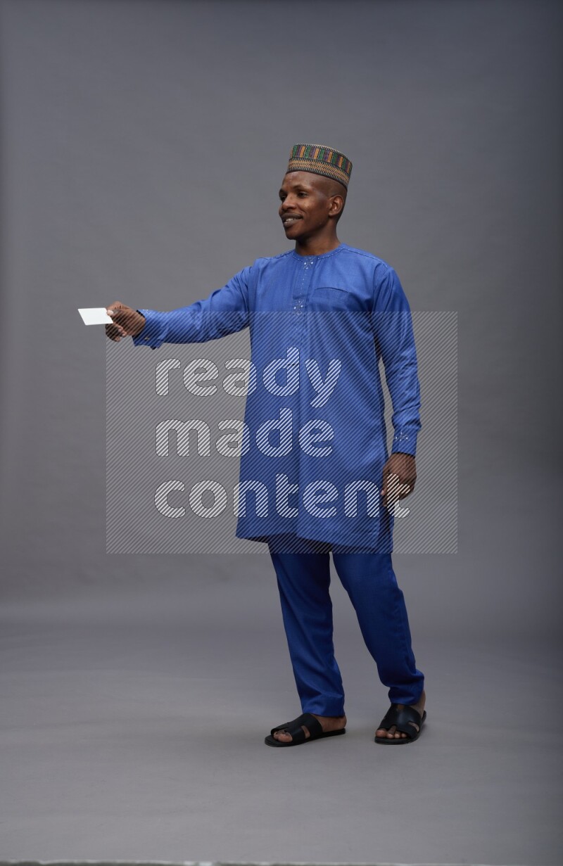 Man wearing Nigerian outfit standing holding ATM card on gray background
