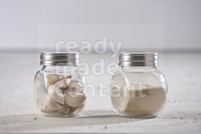 2 glass spice jars one full of garlic powder and the other full of cloves on a textured white flooring