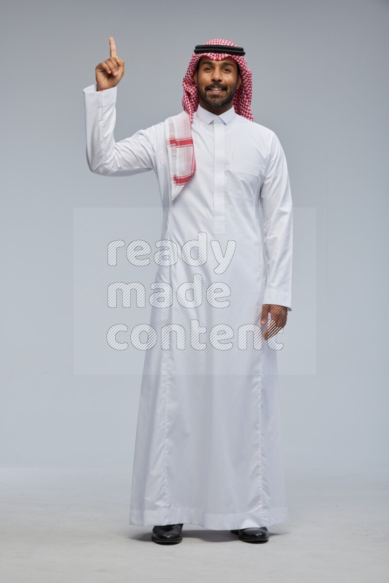 Saudi man Wearing Thob and shomag standing interacting with the camera on Gray background