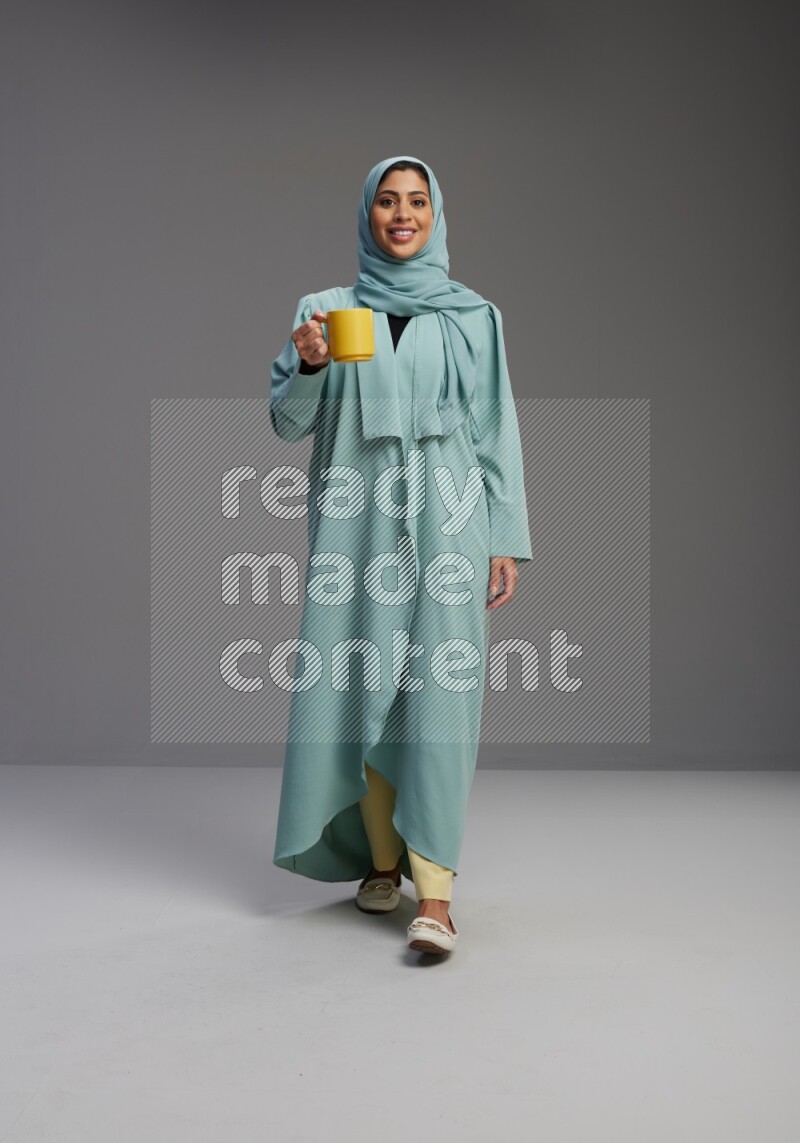 Saudi Woman wearing Abaya standing  holding a mug on Gray background