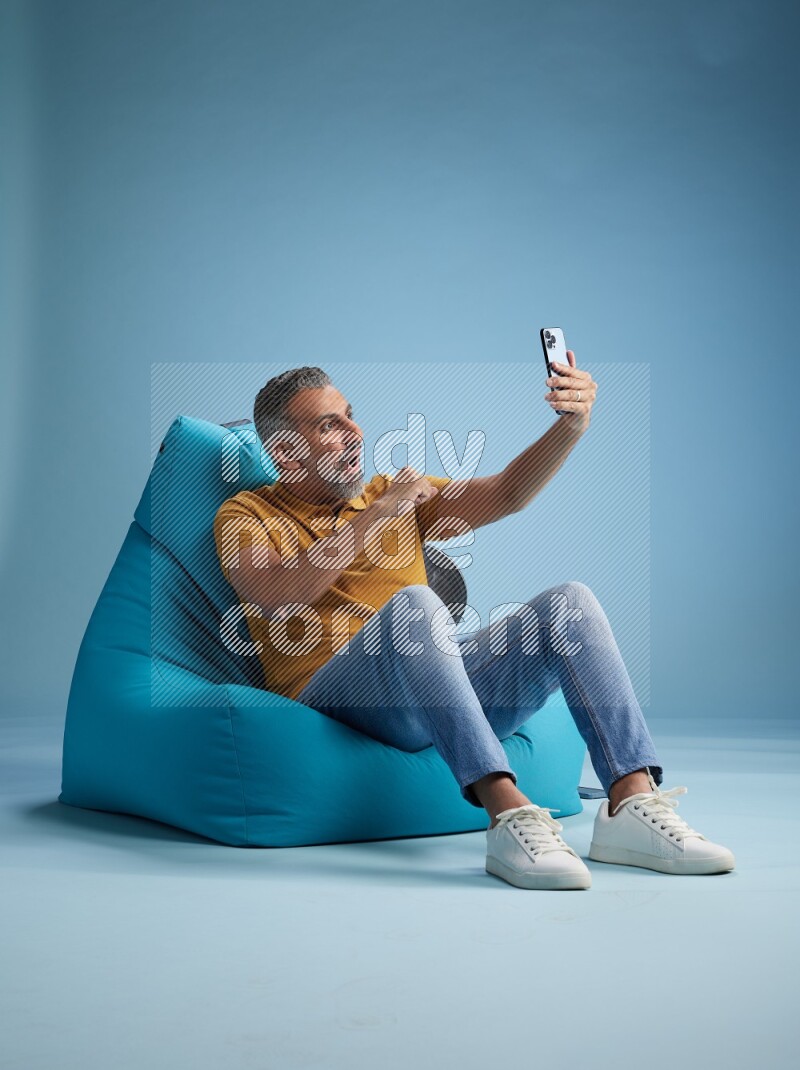 A man sitting on a blue beanbag and taking selfie