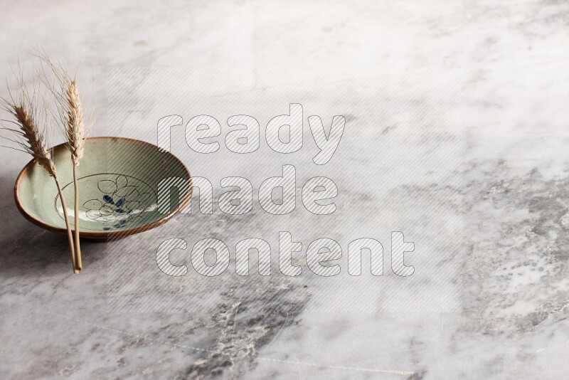 Wheat stalks on decorative pottery plate on grey marble background