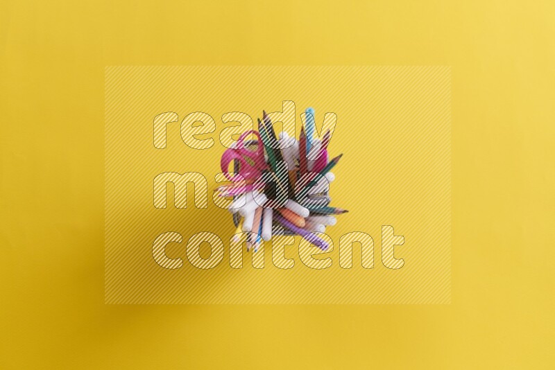 بعض الأقلام والمستلزمات المدرسية في مقلمة معدنية علي خلفية صفراء