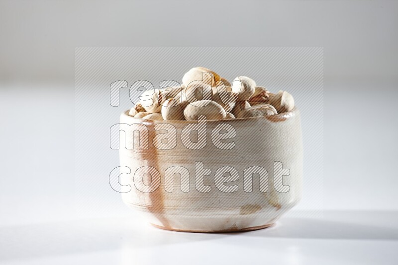 A beige ceramic bowl full of pistachios on a white background in different angles