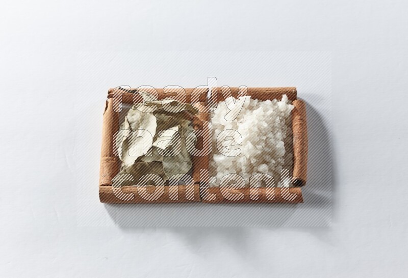 مربعان من أعواد القرفة ممتلئان بالملح الأبيض وأوراق الغار علي خلفية بيضاء