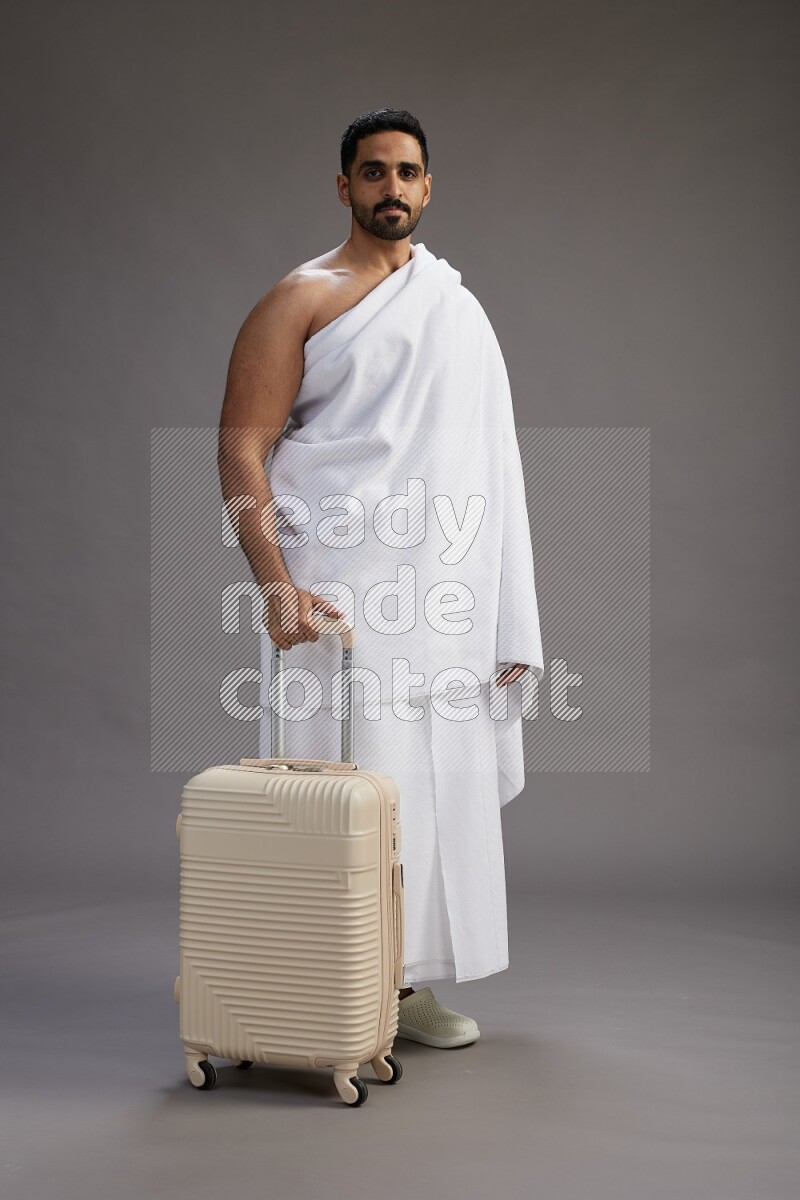 A man wearing Ehram Standing holding traveling bag on gray background
