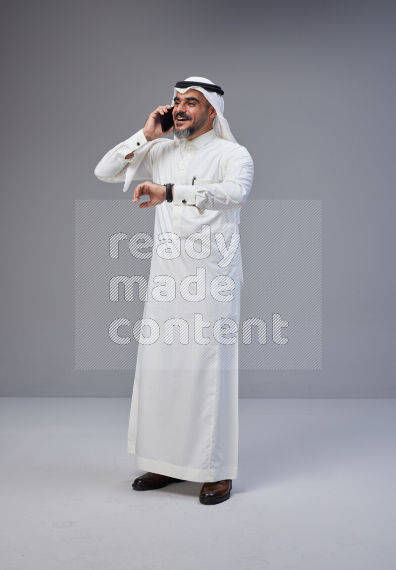 Saudi man Wearing Thob and white Shomag standing talking on phone on Gray background