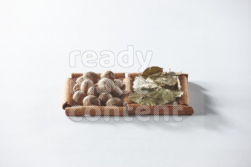 مربعان من أعواد القرفة ممتلئان بأوراق الغار وجوزة الطيب علي خلفية بيضاء