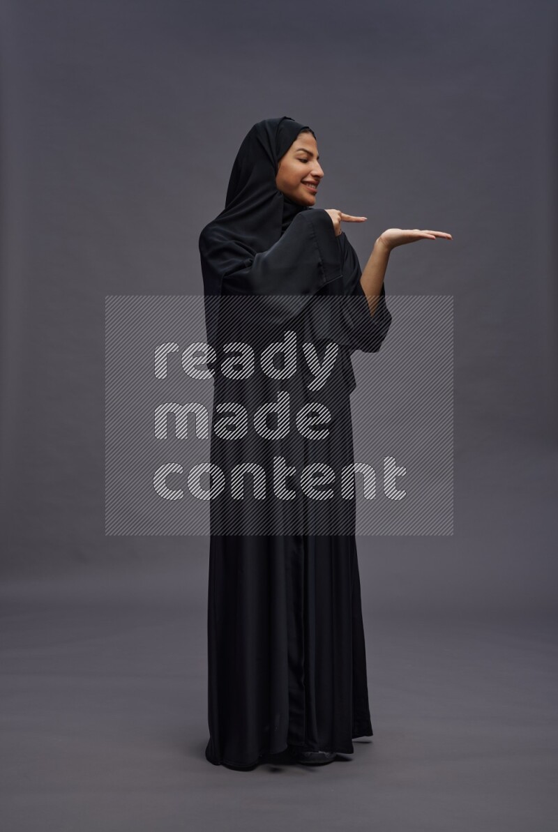 Saudi woman wearing Abaya standing interacting with the camera on gray background