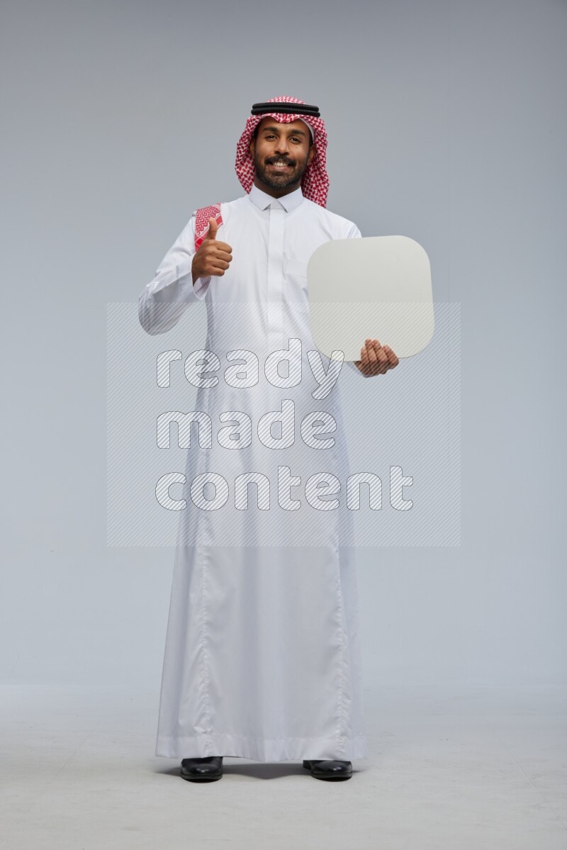 Saudi man Wearing Thob and shomag standing holding social media sign on Gray background