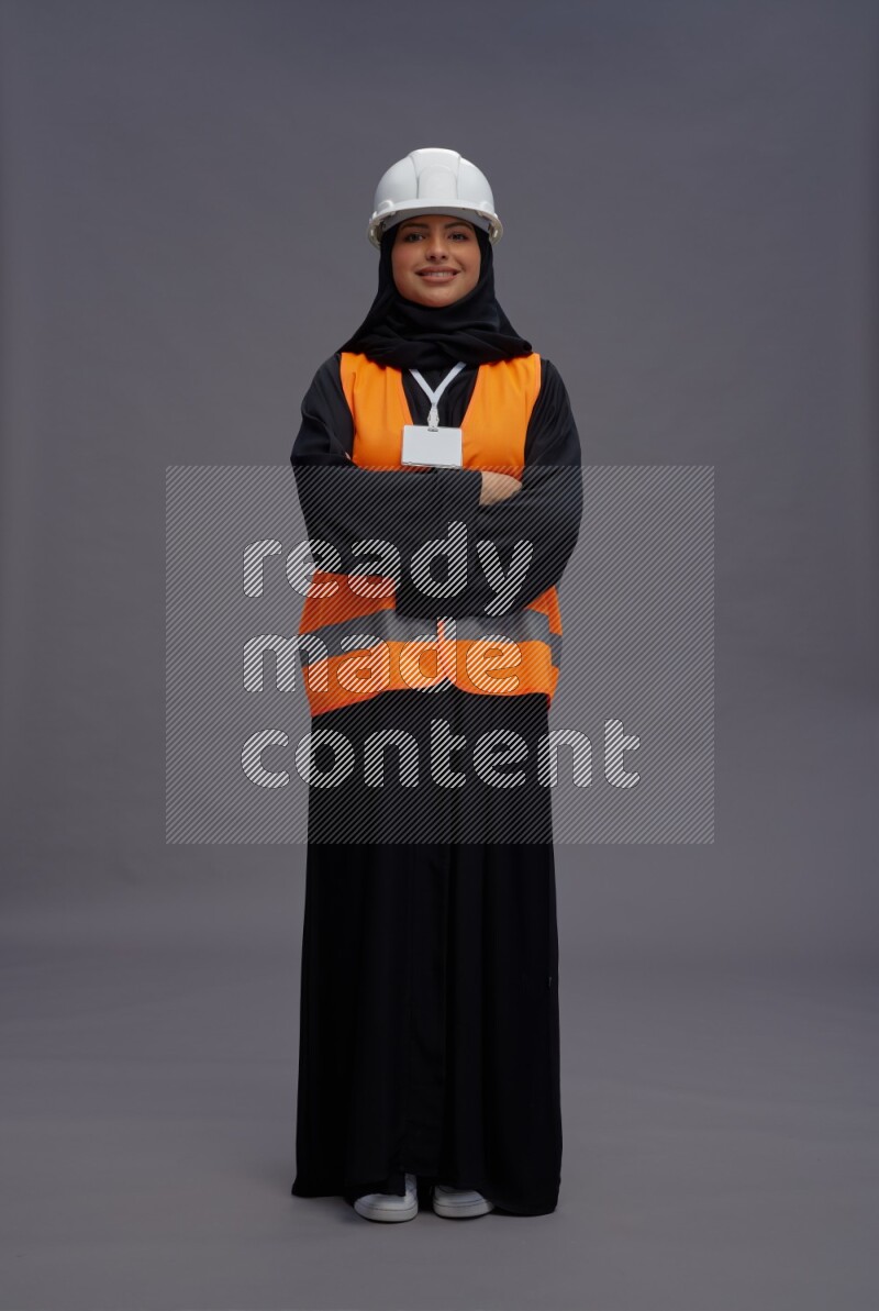 Saudi woman wearing Abaya with engineer vest with neck strap employee badge standing with crossed arms on gray background