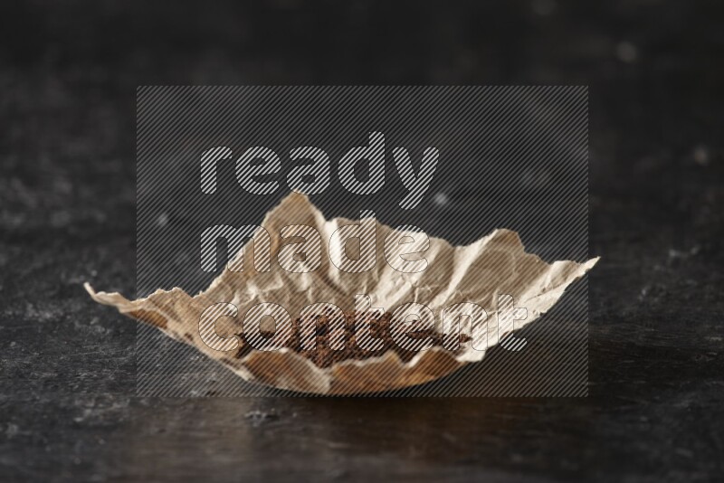 Cloves powder in crumpled piece of paper on a textured black flooring