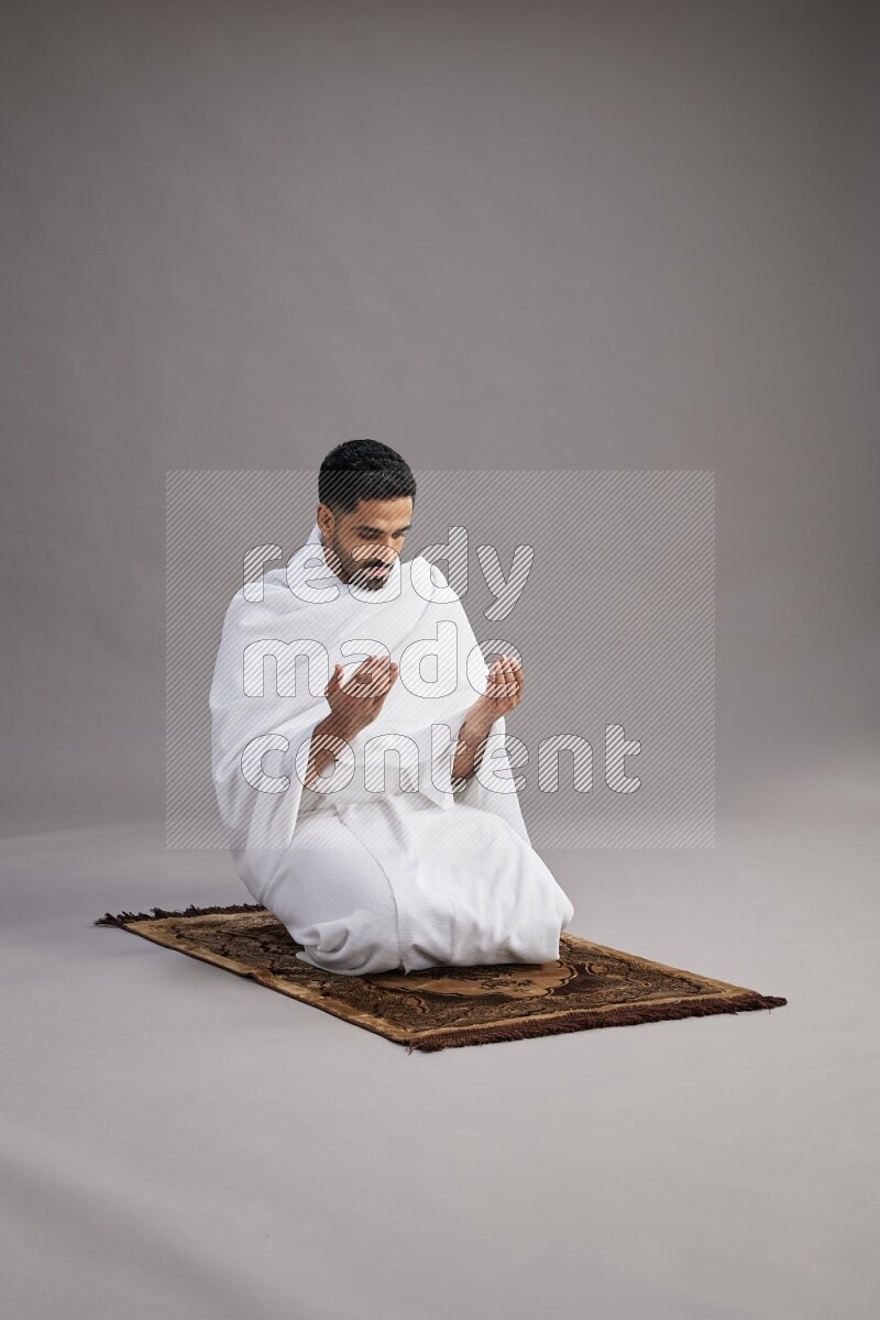 A man wearing Ehram performing dua'a on gray background