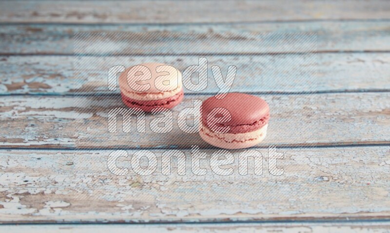 45º Shot of two Pink Litchi Raspberry macarons on light blue wooden background
