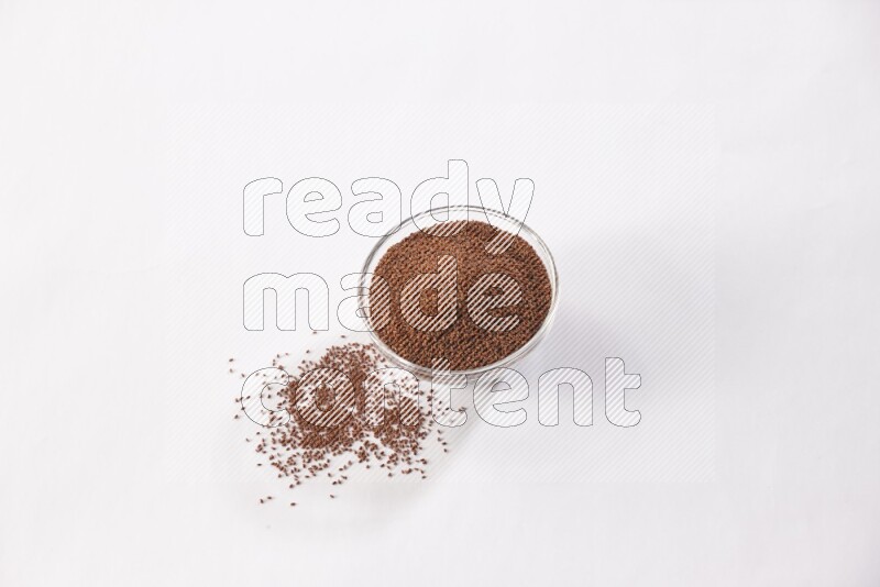 A glass bowl full of garden cress seeds with more seeds spread on a white flooring