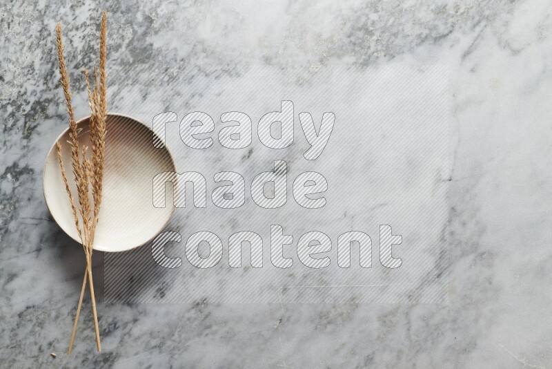 Wheat stalks on beige pottery plate on grey marble background
