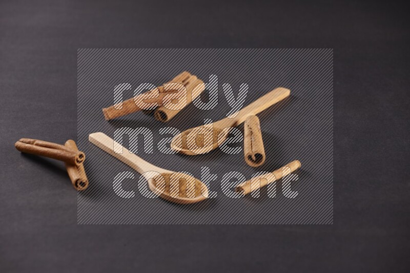 Two wooden spoons full of cinnamon powder with cinnamon sticks on black background