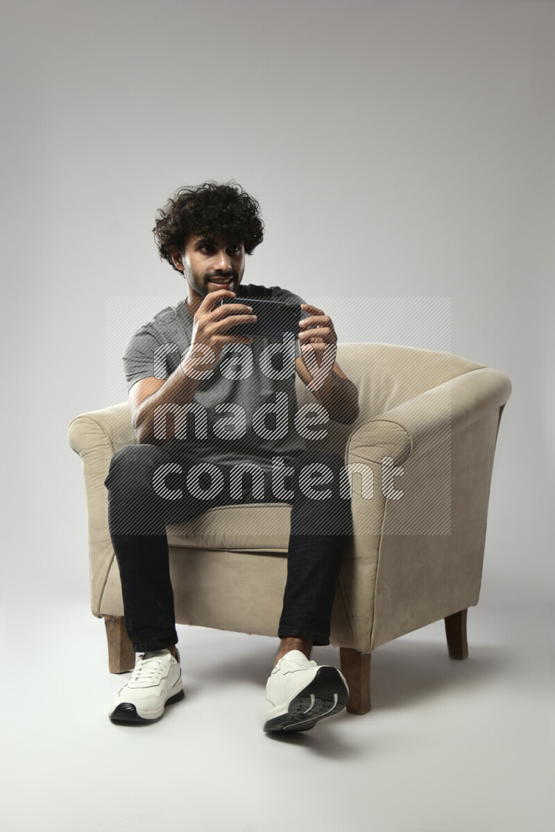 A man wearing casual sitting on a chair shooting with his phone on white background
