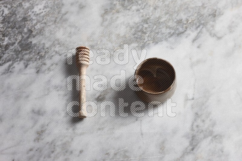 Multicolored pottery bowl with wooden honey dipper on the side on grey marble background