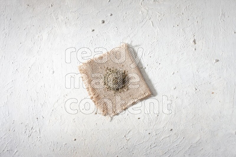 Cumin seeds on a burlap piece on a textured white flooring