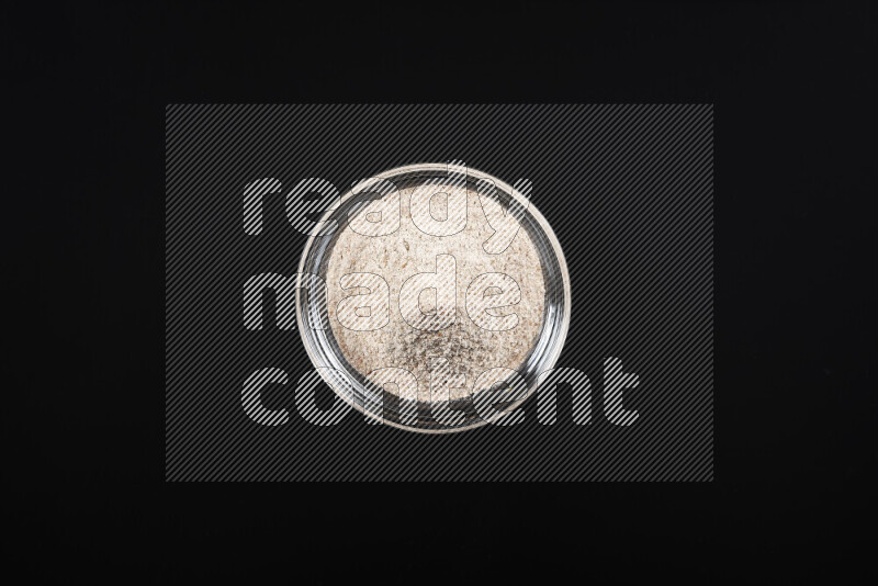 A glass bowl full of onion powder on black background