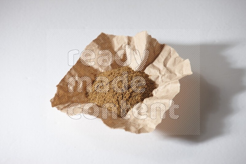 Cumin powder in a crumpled piece of paper on white flooring