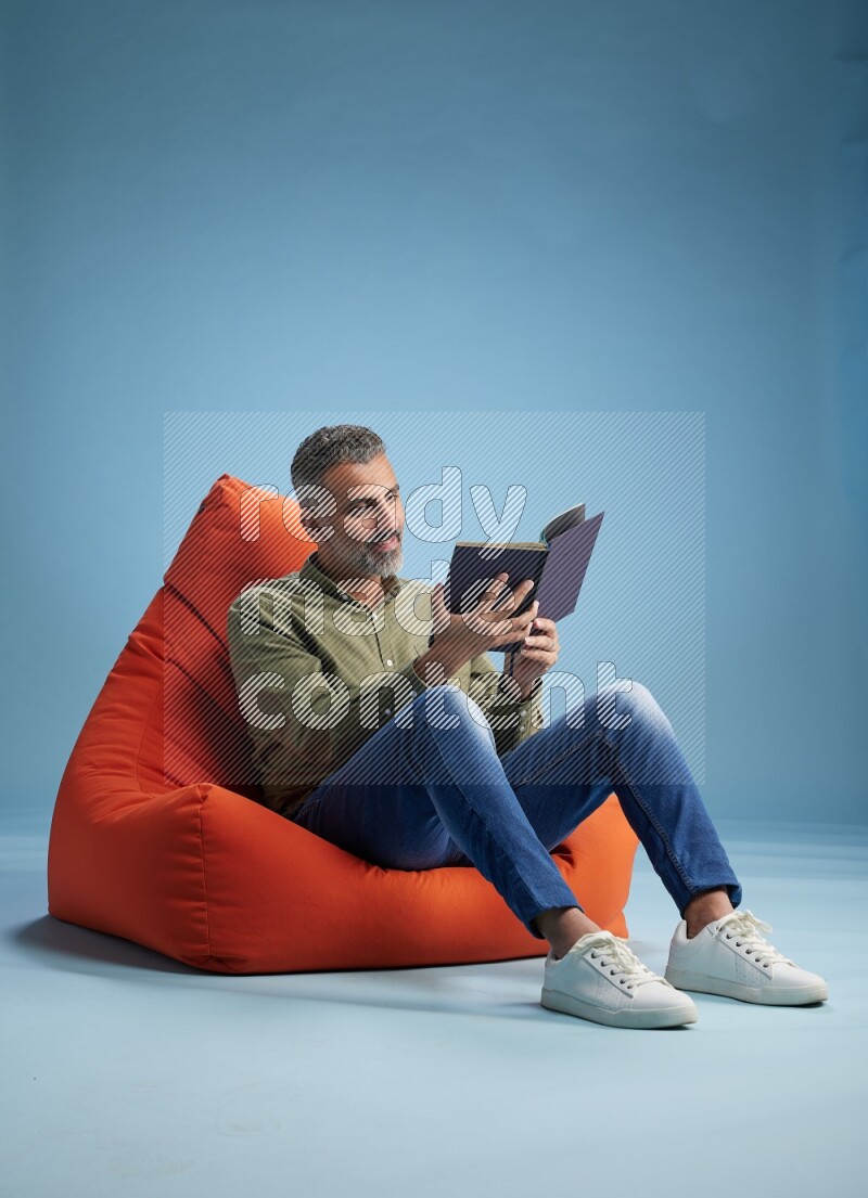A man sitting on an orange beanbag and reading a book
