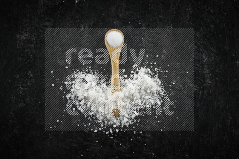 A wooden spoon full of white salt on black background