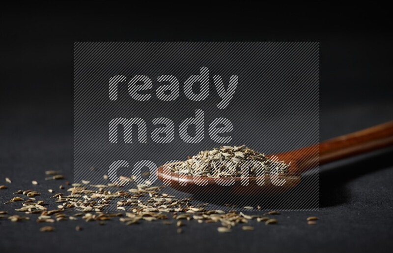 مغرفة خشبية ممتلئة بحبوب الكمون على خلفية سوداء