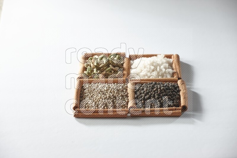 4 مربعات من أعواد القرفة ممتلئة بالهيل والملح والفلفل الأبيض والفلفل الأسود على أرضية بيضاء