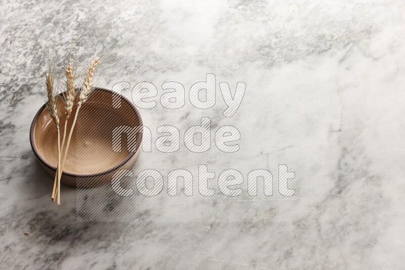 Wheat stalks on beige pottery oven bowl on grey marble background