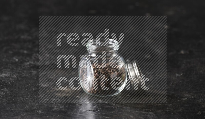 A glass spice jar full of cloves on textured black flooring