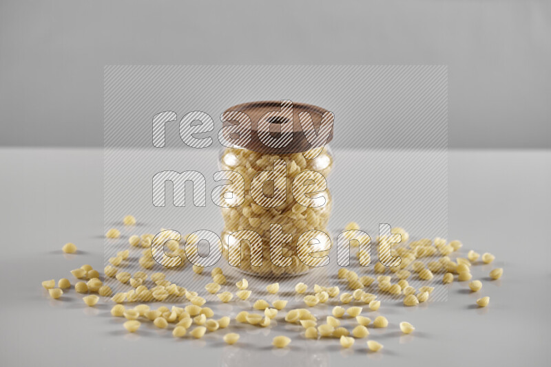 Raw pasta in a glass jar on light grey background