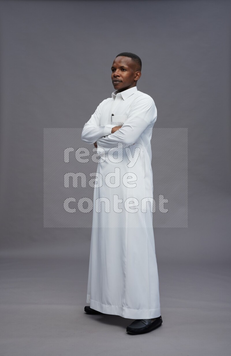 Saudi man wearing thob standing with crossed arms on gray background