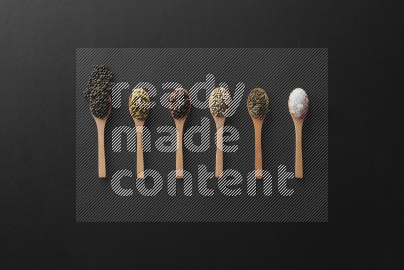 wooden spoons filled with white peppers, cloves, cardamom, salt, black peppers and basil on black flooring