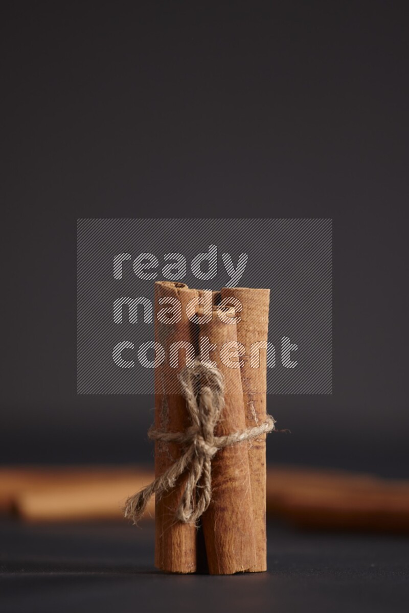 4 Cinnamon sticks stacked and bounded with more sticks in the background on black flooring